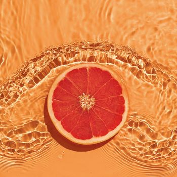 Grapefruit citrus fruit in fresh water with waves on bright background. The concept of summer freshness and healthy nutrition with vitamins.