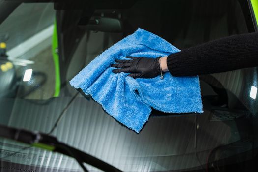 Polishing the car glass with a blue microfiber cloth.