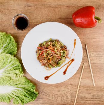 Chinese noodles with seafood in soy sauce and vegetables on a white plate