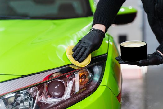 Hard wax for protection paintwork of car using sponge for remove paint scratches. Applying hard wax with a yellow sponge. Protection of paintwork.
