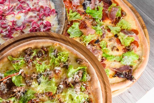 Assortment of pizzas with meat, salami, prosciutto, tomatoes, mozzarella, parmesan, salad, blue onion, quail egg on wooden boards. Top view.