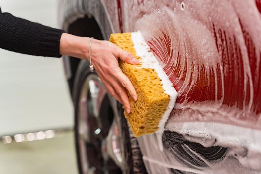 Washing a red car with a foamy yellow sponge. Woman's hand washing a car at the car wash.