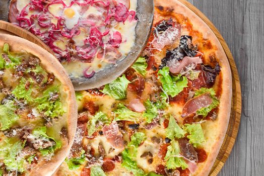 Assortment of pizzas with meat, salami, prosciutto, tomatoes, mozzarella, parmesan, salad, blue onion, quail egg on wooden boards. Top view.
