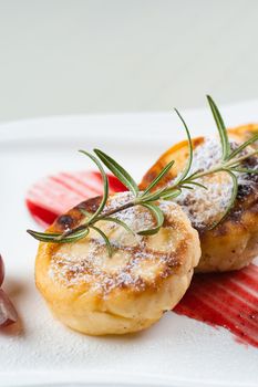 Cheesecakes decorated with powdered sugar, rosemary branch and grapes with berry jam on a white plate. Delicious cottage cheese breakfast.