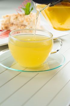 A waiter pours orange tea from a teapot into a transparent cup against the background of a napoleon cake decorated with mint and berry jam on a white wooden table