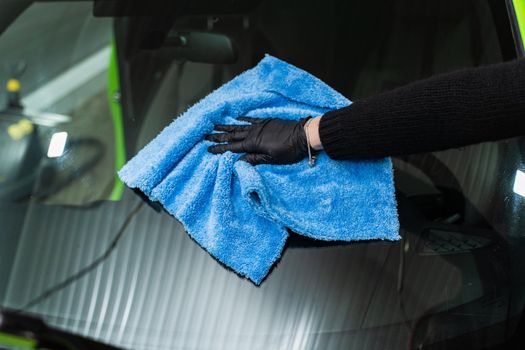 Polishing the car glass with a blue microfiber cloth.