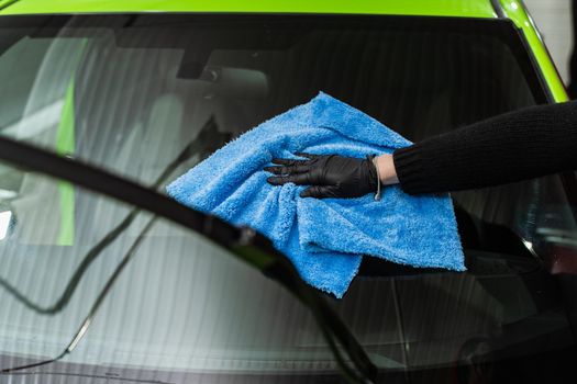 Polishing the car glass with a blue microfiber cloth.