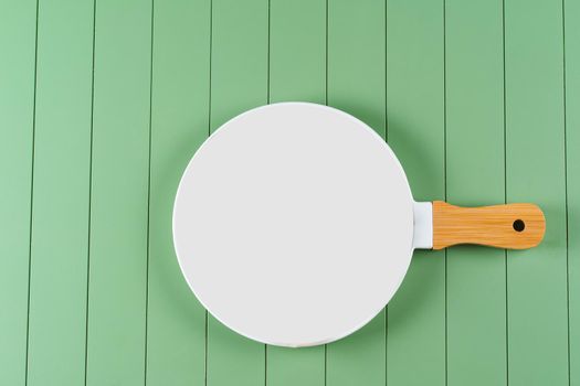 White empty ceramic food pan on green wooden background. White plate on table