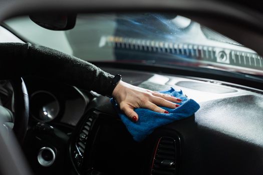 Hand with blue microfiber cloth cleaning interior car.