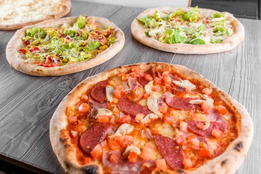 Assortment of pizza with meat, salami, prosciutto, tomatoes, dorblu cheese, mozzarella, parmesan and salad, spinach, red fish on wooden boards. Four cheese pizza, caesar, top view