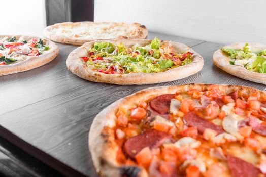 Assortment of pizza with meat, salami, prosciutto, tomatoes, dorblu cheese, mozzarella, parmesan and salad, spinach, red fish on wooden boards. Four cheese pizza, caesar, top view.