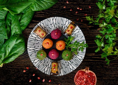 Assortment of pkhali from beets, spinach, carrots, eggplant rolls garnished with parsley and pomegranate . Georgian appetizer on a black and white plate with spinach and parsley leaves. Top view.