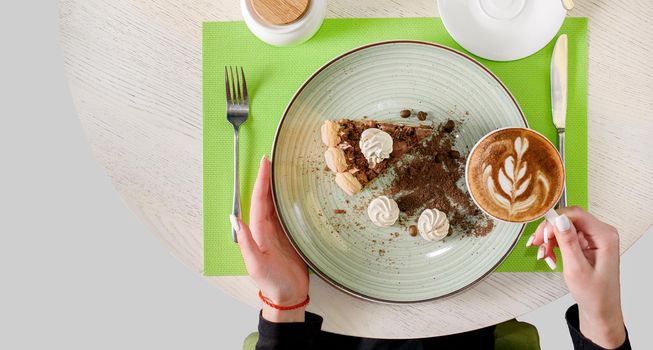 A piece of chocolate cake decorated with meringues, coffee beans and biscuit crumbs, holding a cappuccino in hand. Dessert tiramisu , top view.
