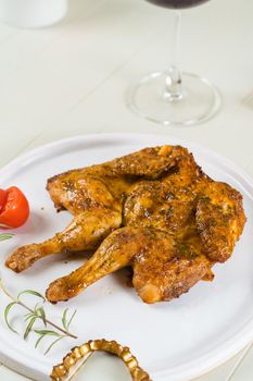 Tobacco chicken on a white plate with a glass of red wine, cutlery. Grilled chicken.