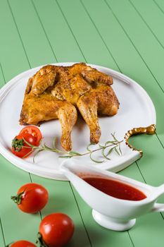 Chicken tobacco with tomato sauce, rosemary and tomatoes on a beautiful white plate on a green background. Grilled chicken.