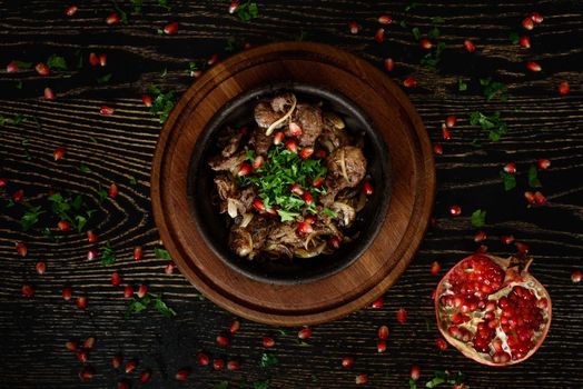 Barbecue meat with onions in a clay plate on a wooden board on a dark wooden table decorated with pomegranate and cilantro. Beautiful table setting.