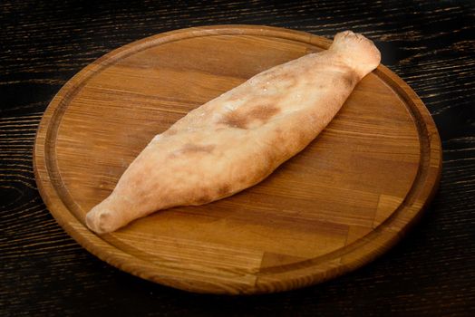 Closed khachapuri with filling on a wooden board on a dark wooden table. Georgian pastries.
