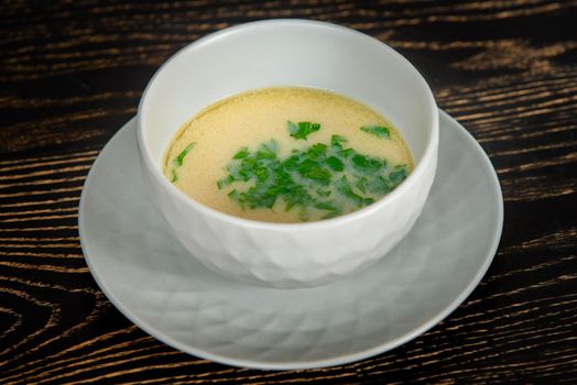 Creamy soup decorated with herbs in a gray bowl on a plate on a dark wooden table.