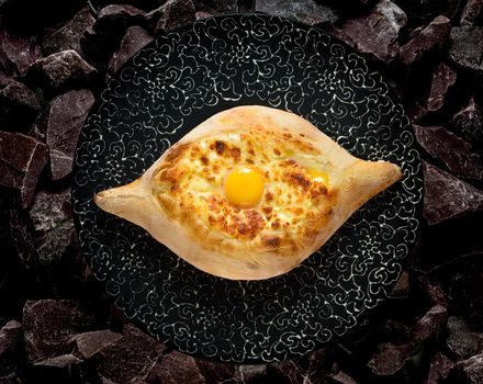 Adjarian georgian khachapuri with egg and cheese national traditional cuisine on a black plate on a background of stones.