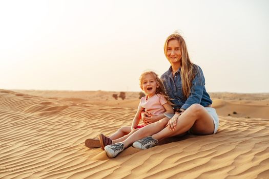 Mother and daughter sitting together on sand dune in the Dubai desert, travel with children concept
