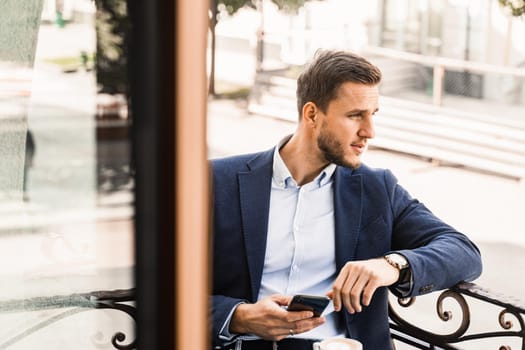 Business is working online using phone. Remote work. Handsome man in cafe on summer terrace