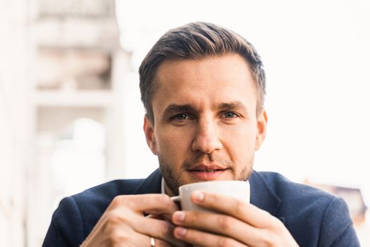 Man like coffee. Handsome man with cup of coffee in cafe. Morning lifestyle of male. Man is sitting on the summer terrace in cafe, drinking coffee and smiling