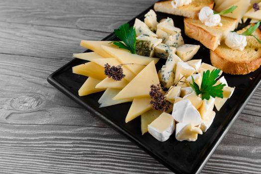 Cheese food board with delicous cheeses, walnuts. Parmesan, jam, dorblu on the black plate. Food appetizer from restaurant