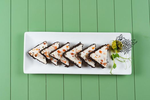 Beautiful snacks of soft cream cheese on a white plate on a green background. Cottage cheese snacks with salmon and herbs.