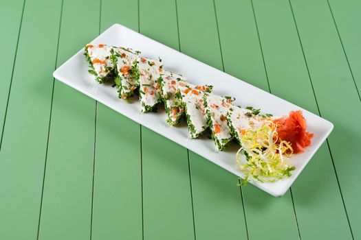 Beautiful snacks of soft cream cheese on a white plate on a green background. Cottage cheese snacks with salmon and herbs.