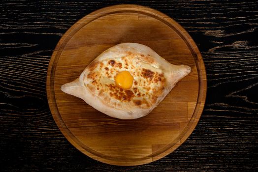 Adjarian georgian khachapuri with egg and cheese national traditional cuisine on a black plate on wooden background