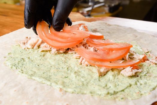 Burrito cooking process. Cook adds tomato to meat on pita with sauce. Mexican dish.