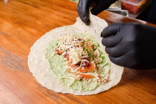 Burrito making process. The chef wraps stuffed pita on a wooden table. Mexican dish.