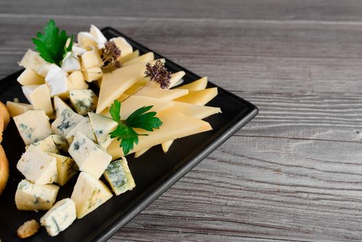 Cheese food board with delicous cheeses, walnuts. Parmesan, jam, dorblu on the black plate. Food appetizer from restaurant