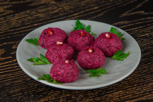 Beetroot phali garnished with parsley and pomegranate. Georgian appetizer on a gray plate on a dark wooden table.