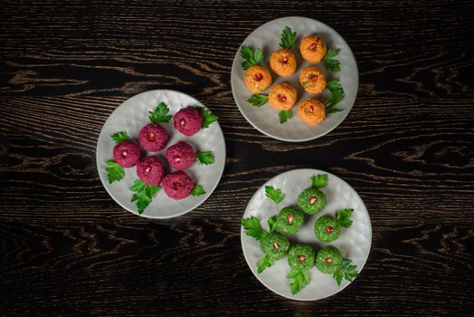 Assortment of pkhali from beets, spinach, carrots, garnished with parsley and pomegranate. Georgian appetizer on a gray plate on a dark wooden table. Top view.