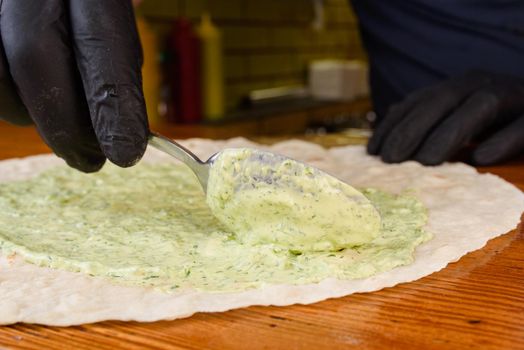 Burrito cooking process. The cook spreads the pita with sauce. Mexican dish.