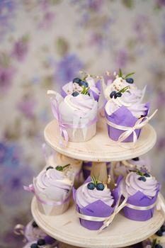 Cupcakes with cream in a paper tulip form, decorated with blueberries, rosemary, flowers, tied with a ribbon. Vanilla cupcakes with lavender cream. Thematic muffins.