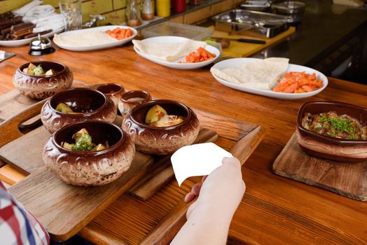 Baked potatoes in ceramic pots with sauce and cheese on wooden board on the background of a restaurant kitchen and cooking. The waiter takes the prepared dish from the kitchen.