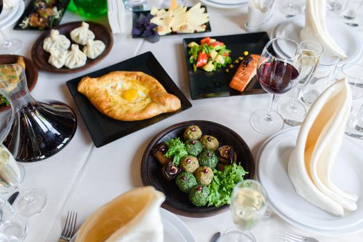 Assortment of dishes phali, khachapuri, khinkali, vegetables table setting bowl with wine, glasses, dishes, napkins.