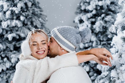 Couple seat on the snow and hug, kiss, and have fun each other. Winter love story before new year celebration. Waiting for christmas gift. Happy couple weared fur headphones, hats, white sweaters.