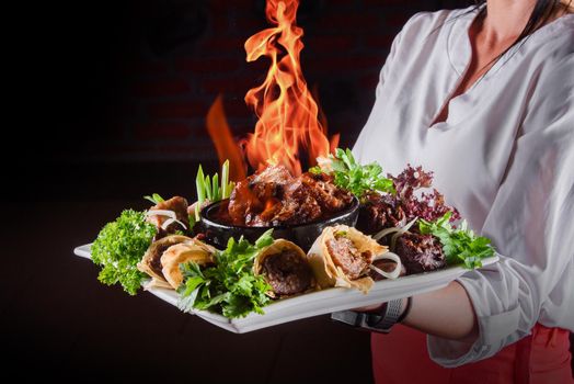 Flame meat in a clay bowl. Meat with fire on plate with grilled vegetables, kebab in pita bread decorated with herbs.