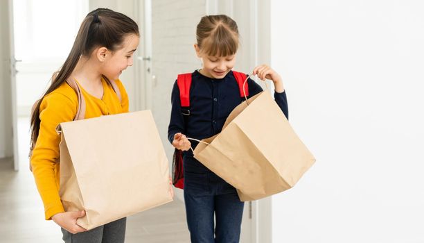 two school girls with backpack and delivery packages hands in white background.