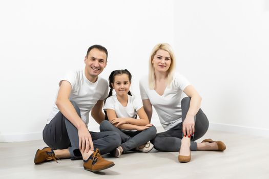 happy family father mother and children sitting on the floor in an empty white wall.
