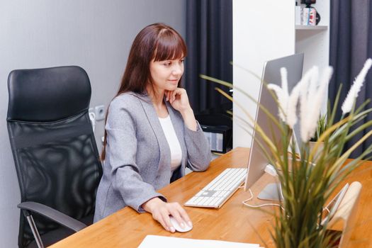 A brunette woman at a computer in the workplace. Business concept.