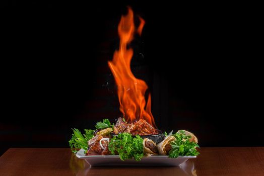 Flame meat in a clay bowl. Meat with fire on plate with grilled vegetables, kebab in pita bread decorated with herbs.