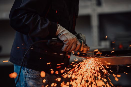 Heavy Industry Engineering Factory Interior with Industrial Worker Using Angle Grinder and Cutting a Metal Tube. Contractor in Safety Uniform and Hard Hat Manufacturing Metal Structures. High-quality photo