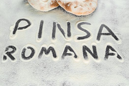 Dough and flour with text pinsa romana on black background. Scrocchiarella gourmet italian cuisine. Traditional dish in italy