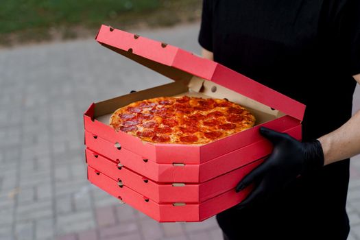 Safety pizza delivery from restaurant. Food courier in black medical gloves. Isolated photo of pizza with cheese and salami. Stop pandemic coronavirus covid 19.