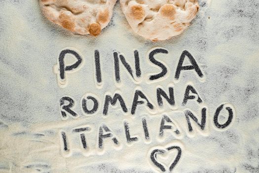 Dough and flour with text pinsa romana italiano on black background. Scrocchiarella gourmet italian cuisine. Traditional dish in italy