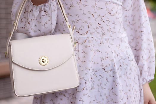 close up of woman in white dress holding fashionable beige purse outside. Product photography. stylish handbag for women.